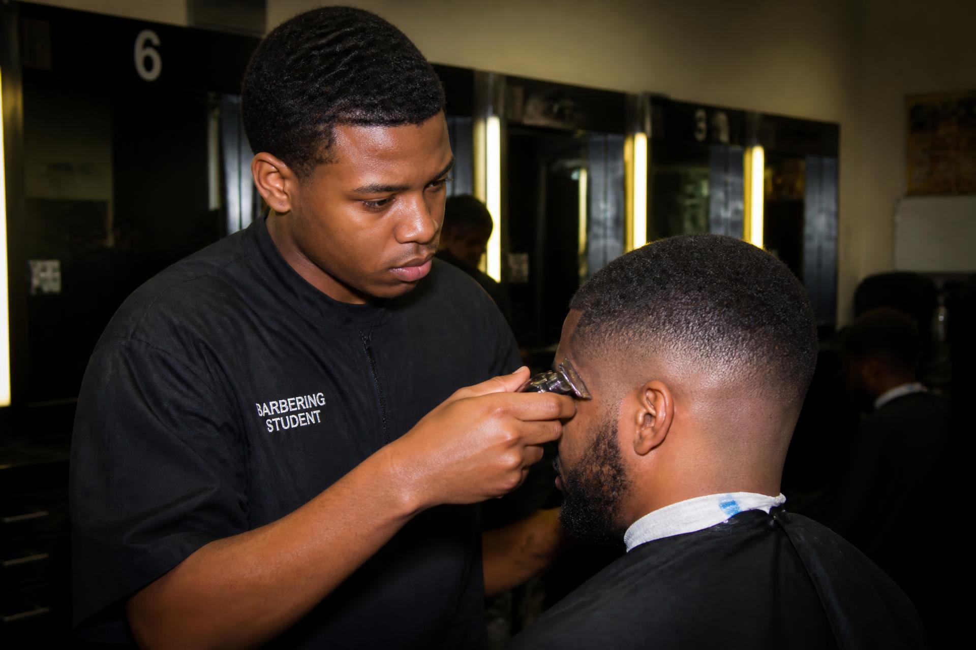 Barbering student finishing a fade haircut under instructor supervision